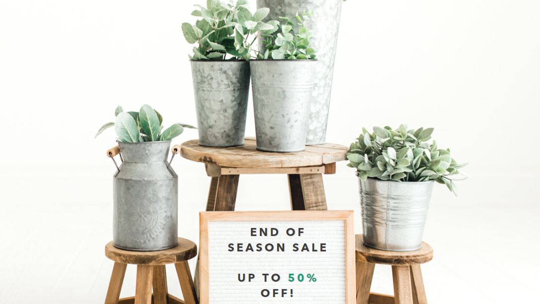 An image of potted plants. In front of them, there is a sign that reads as "End of season sale up to 50% off!". 