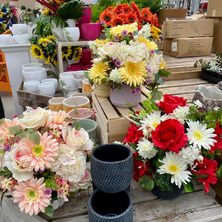 Display of various flower arrangements and pots in a greenhouse setting