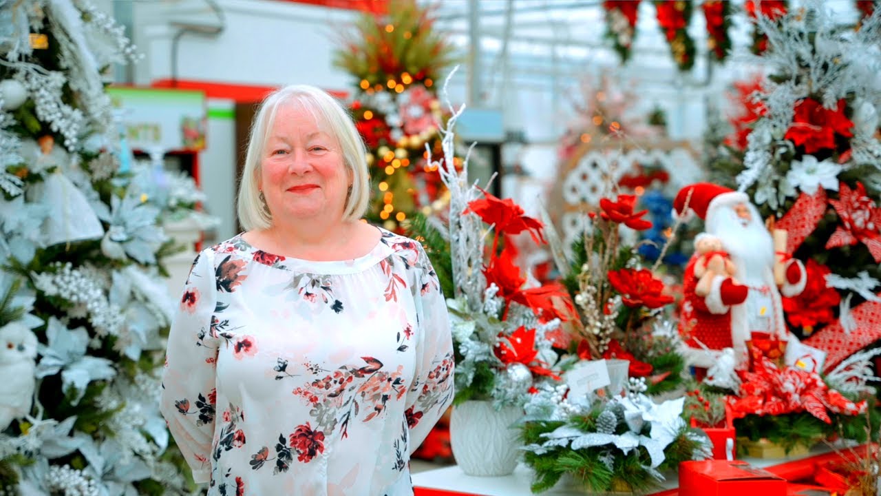 A woman smiling for the camera and standing inside a Greenhouse decorated for Christmas.